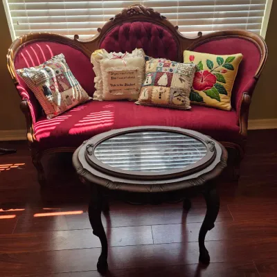 Victorian-style camelback settee with deep red tufted upholstery and carved wood frame, paired with an oval wood coffee table featuring a...