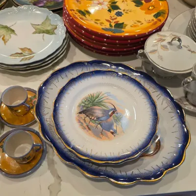 Assorted vintage tableware, featuring a cobalt blue and gold-rimmed plate set with a quail illustration, alongside floral-patterned...