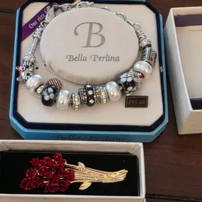 Bella Perlina charm bracelet in its original display box, featuring black, white, and silver-tone beads, alongside a gold-tone and red...