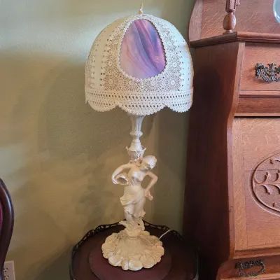 Vintage figural table lamp featuring a white-finished female statue base and a dome-shaped lace shade with a colorful stained glass insert.