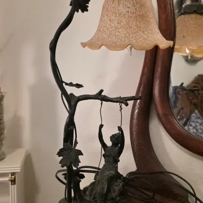 Art Nouveau style bronze-finish table lamp featuring a woman on a swing suspended from a tree branch, complete with a mottled amber glass...