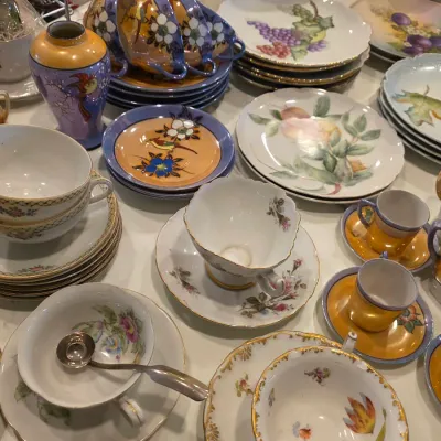 Assortment of vintage porcelain tableware, including floral and fruit-patterned plates, teacups with saucers, and small demitasse cups in...