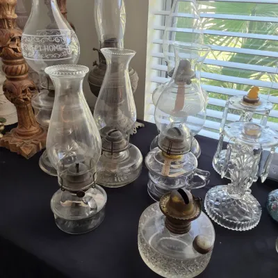 Collection of vintage glass oil lamps and hurricane lamps in various sizes and styles, displayed on a black tabletop.