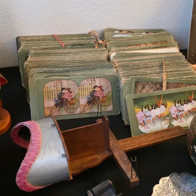 Antique wooden and metal stereoscope viewer with pink trim, accompanied by two large stacks of vintage stereoview cards.