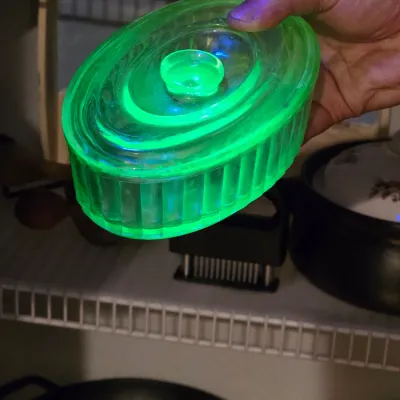 Vintage green uranium glass butter dish with lid, showing a bright fluorescent glow under UV light.