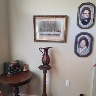 Assorted home decor including a framed print of The Last Supper, vintage oval-framed portraits, a wooden pedestal stand with a decorative...