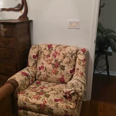 Vintage floral upholstered armchair with rolled arms and a skirted base, positioned next to a wooden dresser.