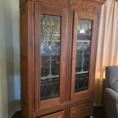 Antique oak armoire or display cabinet featuring double doors with leaded and stained glass panels, carved foliate details on the frieze,...