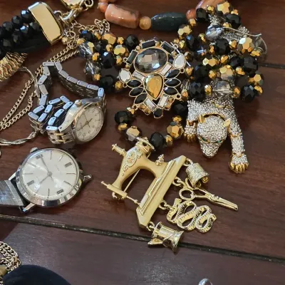 Assortment of vintage costume jewelry and watches, featuring a gold-tone sewing machine brooch with dangling charms, a rhinestone panther...