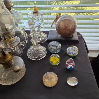 Collection of vintage glass items including oil lamps, crystal candelabras with hanging prisms, and various decorative glass paperweights.