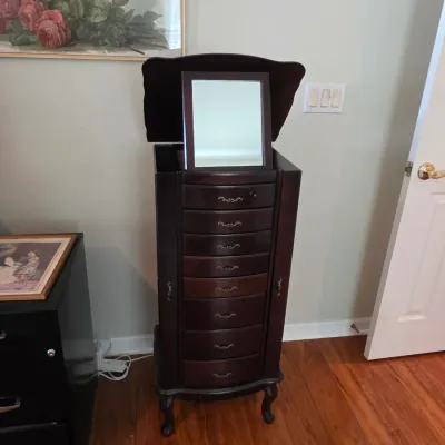 Traditional dark wood jewelry armoire featuring a flip-top mirror, multiple drawers with ornate metal pulls, and cabriole legs.