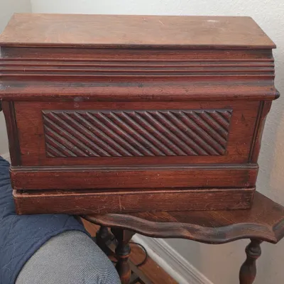 Antique wooden sewing machine case cover with carved diagonal fluting on the front panel, showing some surface wear and scratches.