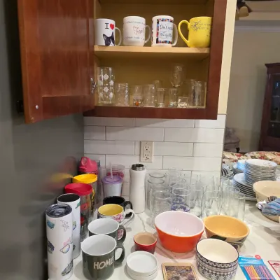 Assorted kitchenware including ceramic mugs, drinking glasses, tumblers, and mixing bowls displayed on a countertop and inside a wooden...