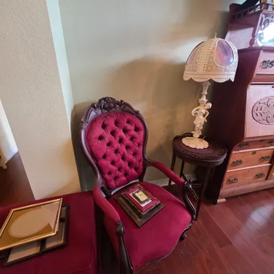 Victorian-style parlor chair with deep red tufted velvet upholstery and carved dark wood frame, paired with a matching footstool and a...