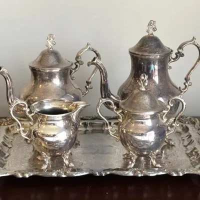 Vintage silver-plated tea and coffee service set, including a teapot, coffee pot, creamer, and sugar bowl, displayed on a matching footed...
