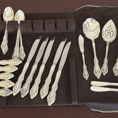 Vintage sterling silver flatware set with ornate floral handles, displayed on brown tarnish-resistant felt rolls.