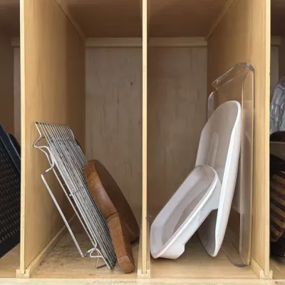 Assorted kitchenware stored in a wooden cabinet organizer, including a black baking sheet, wire cooling rack, wooden cutting boards, and...