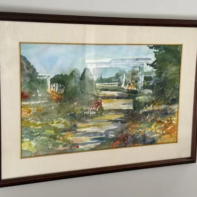 Framed watercolor painting depicting a garden path leading to a white pergola, signed by the artist in the lower right corner and...