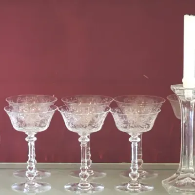 Vintage etched crystal stemware collection, including coupe glasses, a small glass pitcher, and a pair of tall glass candlesticks with...