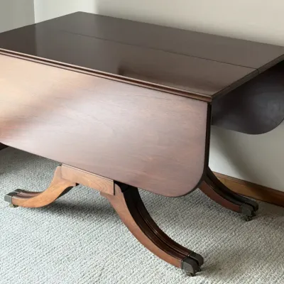 Duncan Phyfe style mahogany drop-leaf table with curved legs on brass casters, showing a polished finish in excellent condition.