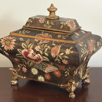 Vintage decorative footed box featuring a hand-painted floral and bird motif on a dark textured background, accented with ornate...
