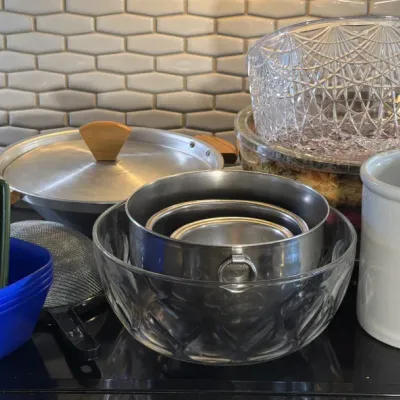 Assorted kitchenware including a white ceramic crock, stainless steel mixing bowls, a clear glass bowl, a vintage aluminum pot with a...
