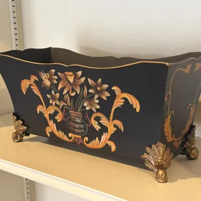 Vintage black metal footed planter featuring hand-painted floral and scrollwork designs in warm gold and orange tones, supported by...