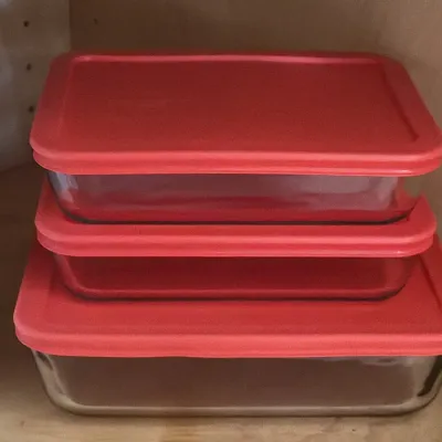 Stack of three Pyrex glass food storage containers with red plastic lids, in various rectangular sizes.