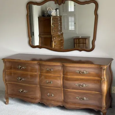 French Provincial style nine-drawer wooden dresser with a matching wall-mounted mirror, featuring ornate brass pulls and curved cabriole...