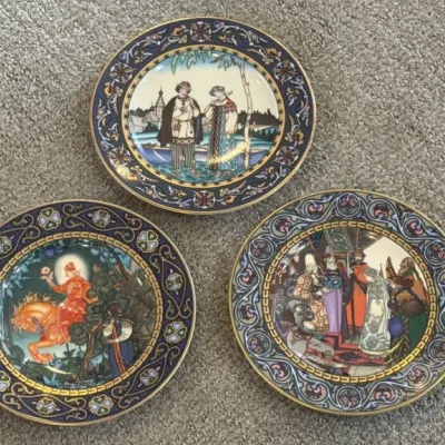 Three vintage Russian porcelain collector plates, featuring detailed illustrations of traditional folklore and fairy tales with ornate...