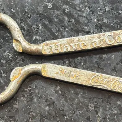Vintage metal Coca-Cola bottle opener with embossed lettering reading "Have a Coke" and "Drink Coca-Cola," showing...