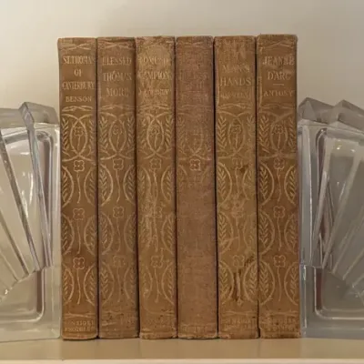 Pair of Art Deco style clear glass fan-shaped bookends holding a set of six vintage cloth-bound books with gilded spines.