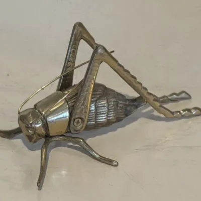 Vintage brass cricket boot jack, featuring movable legs and detailed textured body.