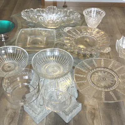 Assorted vintage clear pressed glass serving bowls and platters, including ribbed, floral, and beaded patterns, displayed alongside a...
