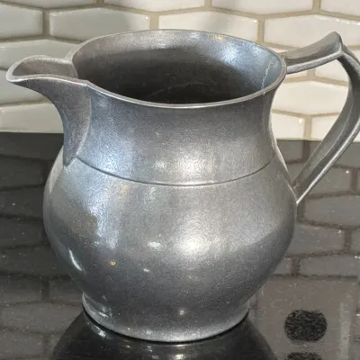 Vintage pewter pitcher featuring a bulbous body, flared rim, and a simple curved handle, displayed on a dark countertop.