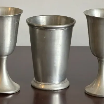 Three vintage pewter drinking vessels, including a pair of stemmed goblets and a central tumbler with beaded rim detailing, showing minor...