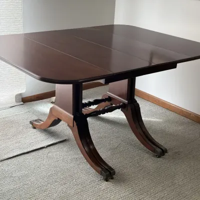 Duncan Phyfe style mahogany dining table featuring a double pedestal base with brass-capped feet and one leaf insert.