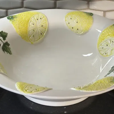Large white ceramic serving bowl featuring raised, hand-painted lemon slices and green leaf details along the rim.