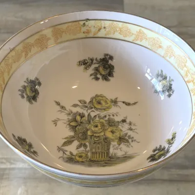Vintage porcelain serving bowl featuring a yellow and grey floral basket motif, accented with a yellow grape leaf border and gold trim.