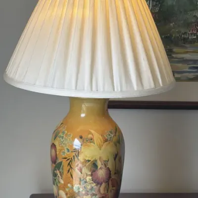Vintage ceramic table lamp featuring a hand-painted floral design on a yellow and gold ground, complete with a pleated cream fabric shade.