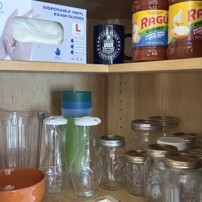 Assorted kitchenware and pantry items, including glass mason jars, carafes, a plastic pitcher, a Washburn University mug, and a box of...