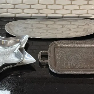 Assorted metal serving ware, including a large oval platter, a textured rectangular tray with handles, and a pair of nested star-shaped...
