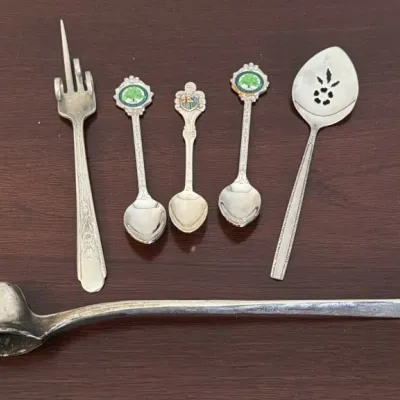 Assorted vintage silver-plated serving utensils and souvenir spoons, including a candle snuffer, a pickle fork, and a pierced serving spoon.