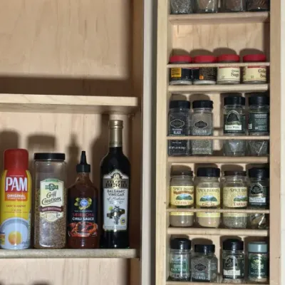 Wooden door-mounted spice rack filled with various spices, shown alongside cabinet shelves holding cooking sprays, sauces, and seasonings.