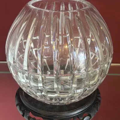 Spherical cut crystal rose bowl featuring vertical and crisscross cuts, displayed on a carved dark wood stand.