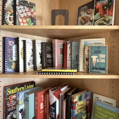Collection of vintage cookbooks and recipe booklets, including spiral-bound community cookbooks and titles like "The I Hate to Cook...
