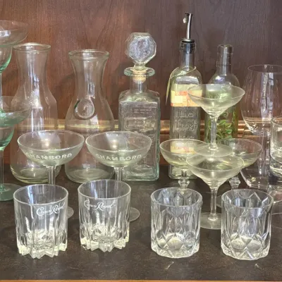 Assorted glassware collection including Crown Royal lowball glasses, Chambord coupe glasses, carafes, a decanter, and margarita glasses.