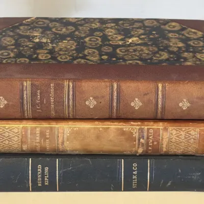 Stack of three antique leather-bound books, including works by J.C. Tuxen, H.F. Ewald, and Rudyard Kipling, featuring marbled paper...
