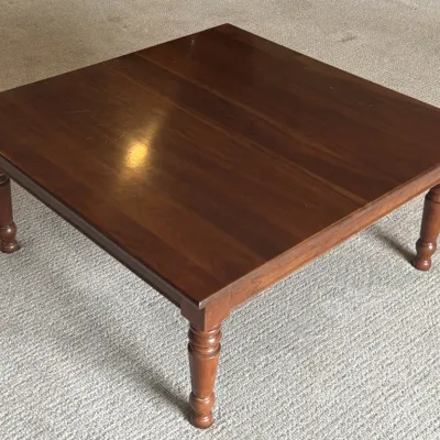 Square wooden coffee table with a dark cherry finish and turned legs, showing minor surface wear.