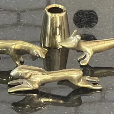 Set of three miniature brass animal figurines, including a fox and a rabbit, alongside a small brass cone, showing a polished finish with...